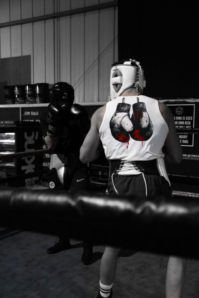 Two boxers sparring in the ring at the Prevail gym, one wearing a white Prevail vest with the boxing gloves graphic across the back
