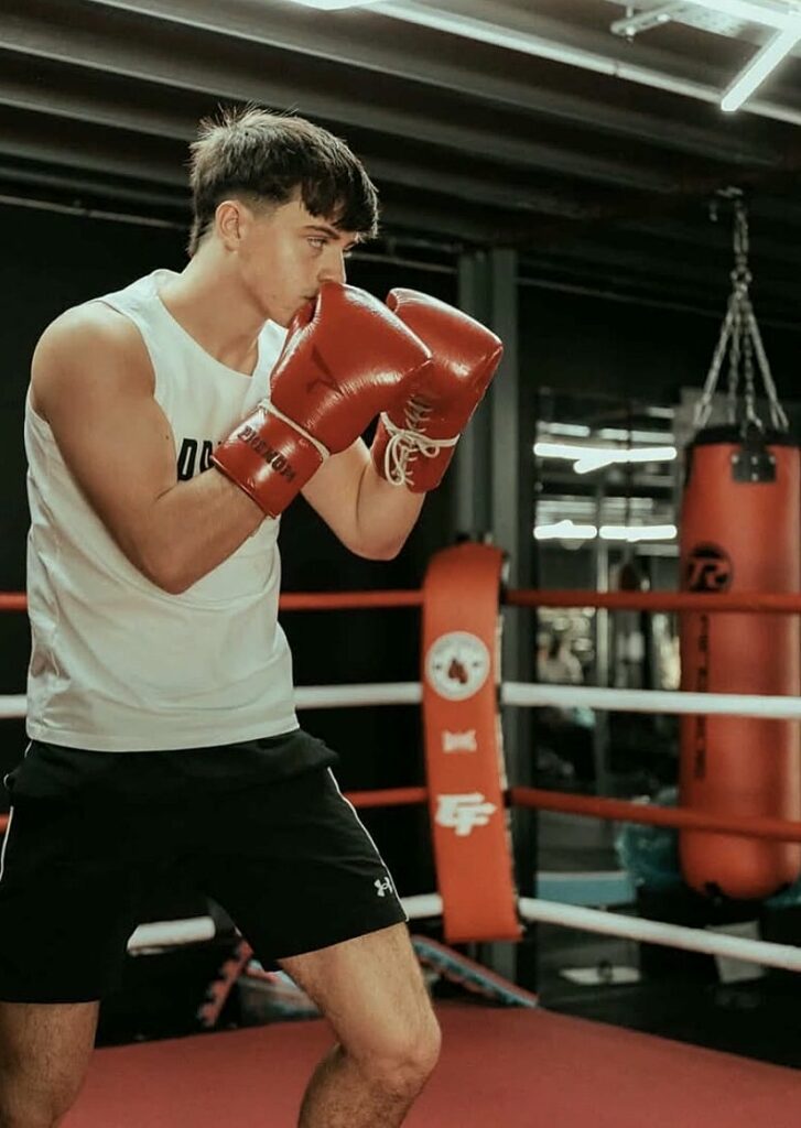 Boxer in a white Prevail vest with red gloves raised in a guard, training in the ring